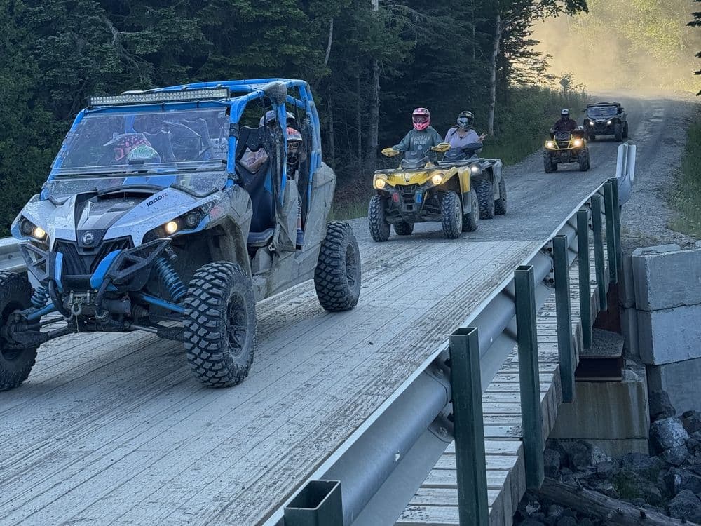 A side-by-side and two ATVs crossing a wooden trail bridge in single file.