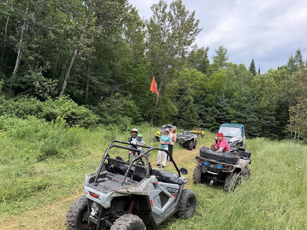 A group of riders stopped in a grassy trail clearing with their ATVs and side-by-sides.