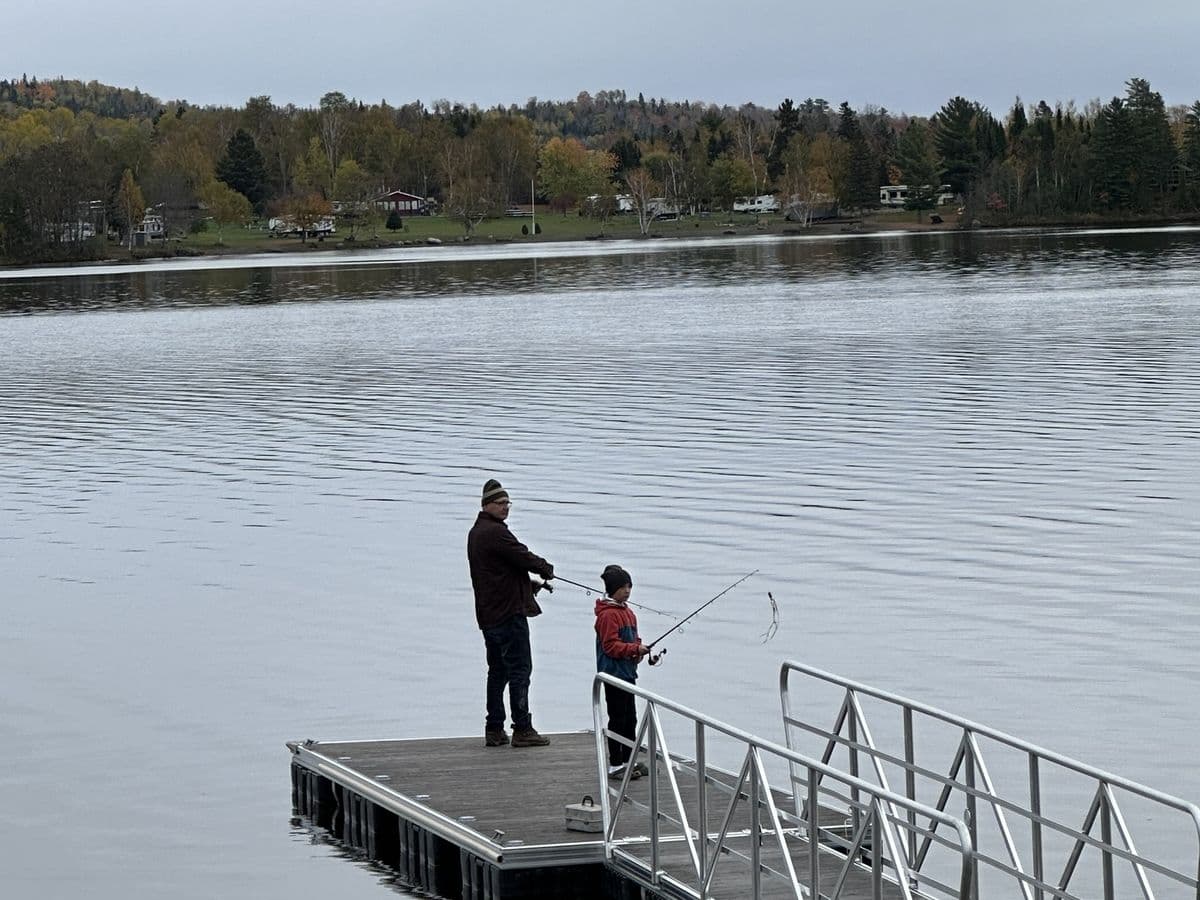 Two people casting off the end of the dock in the fall, with autumn color along the far shore.