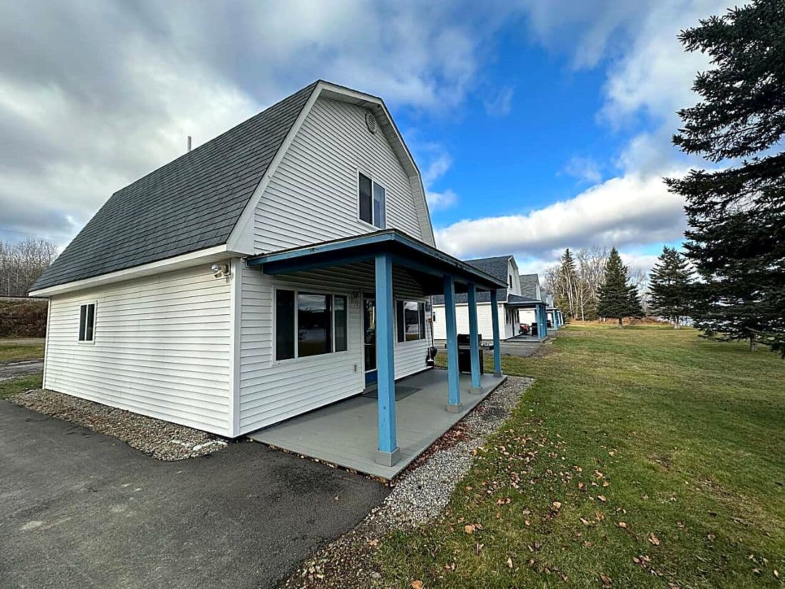 A white cottage with a gambrel roof and blue porch posts, with the other cottages behind it.