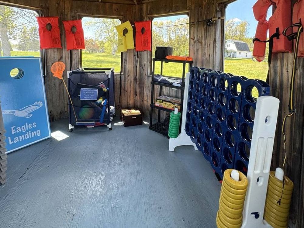 Inside the screened gazebo: giant Connect Four, cornhole boards, life jackets and a cart of toys.