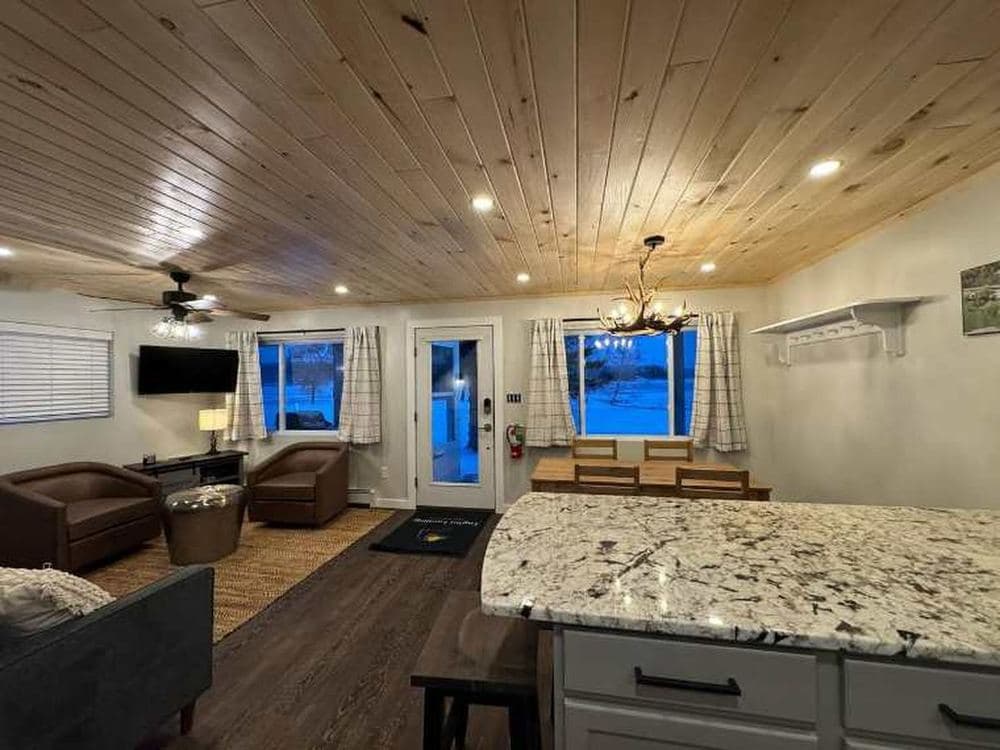 Open-plan cottage interior with pine ceilings, granite counters and a dining area looking out at the lake.