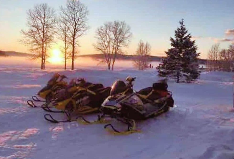 Snowmobiles parked on the snow at sunset beside the cabins at Eagles Landing.