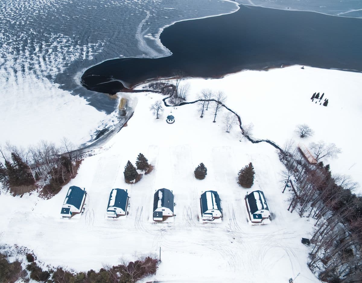 The five cottages under snow seen from the air, with the lake partly frozen beyond.