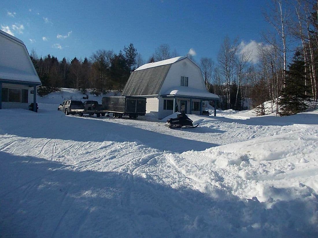 Two of the cabins at Eagles Landing under snow, with a snowmobile parked in the plowed lot.
